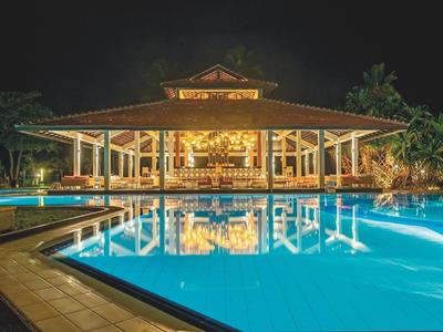 Illuminated resort with large pool and open pavilion at night.