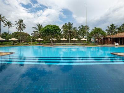 Large hotel pool with palm trees, sun umbrellas, and blue sky in the background.
