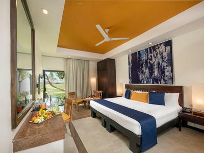 Modern hotel room with large bed, desk, ceiling fan, and balcony overlooking greenery.