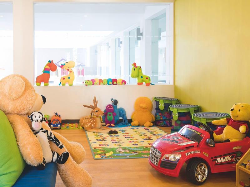 Children's play area with large plush toys and a toy car in a bright room.