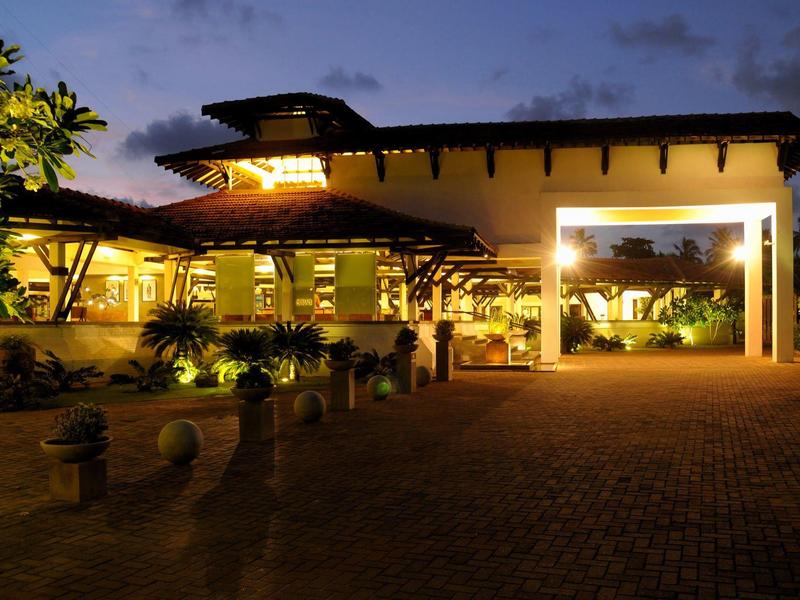 Illuminated hotel entrance at dusk with covered area and plants.