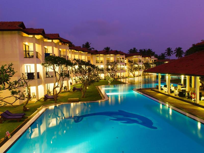 Lit hotel pool with adjacent building and open area at dusk.