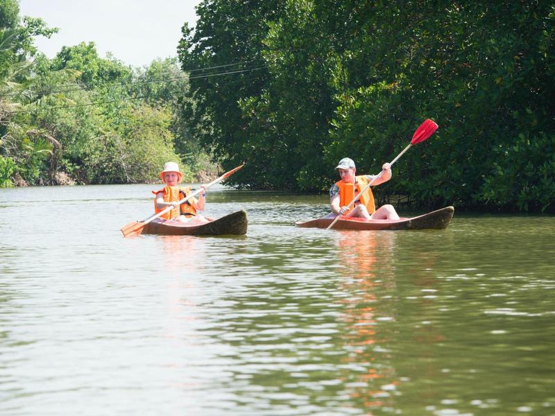 Two people paddling canoes on a calm river with green trees along the banks.