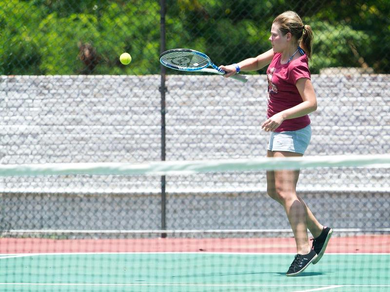 Woman playing tennis on an outdoor court with red and green surface.
