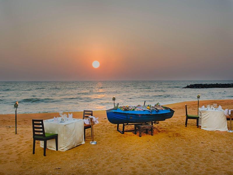 Romantic beach dinner with tables, chairs, and boat at sunset.