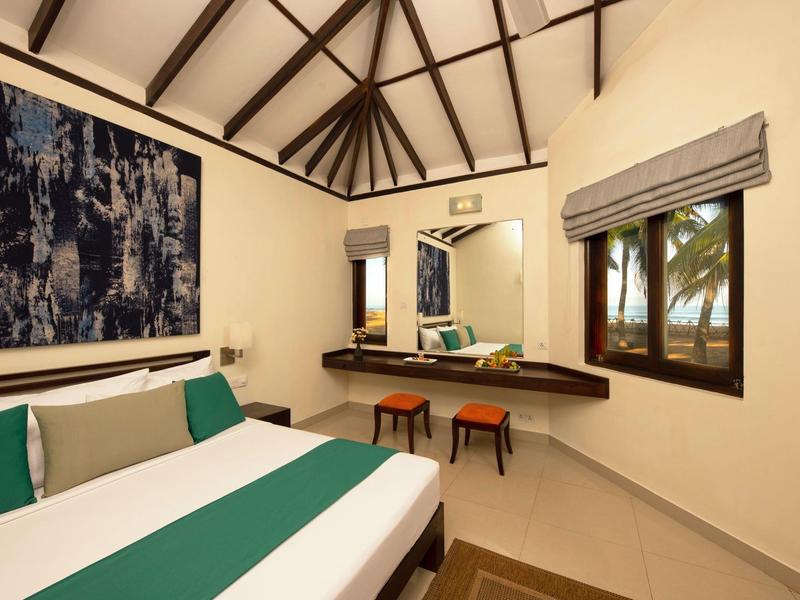 Modern hotel room with high ceiling, large bed, and workspace with two stools.