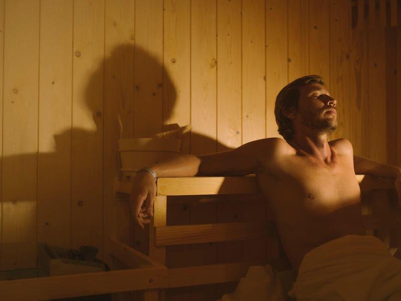 A man relaxes in a sauna with wooden paneling and warm lighting.
