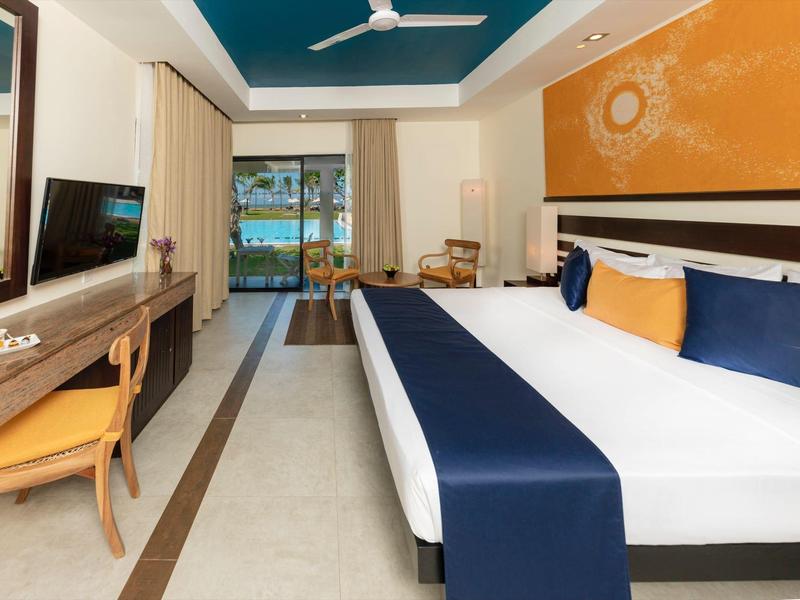 Modern hotel room with large bed, desk, and view of balcony and sea.