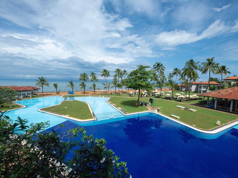 Large pool overlooking palm trees and the sea under a partly cloudy sky.