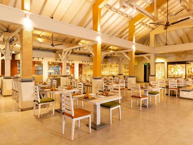 Bright restaurant with wooden beams, tables, and chairs, warmly lit and spacious.