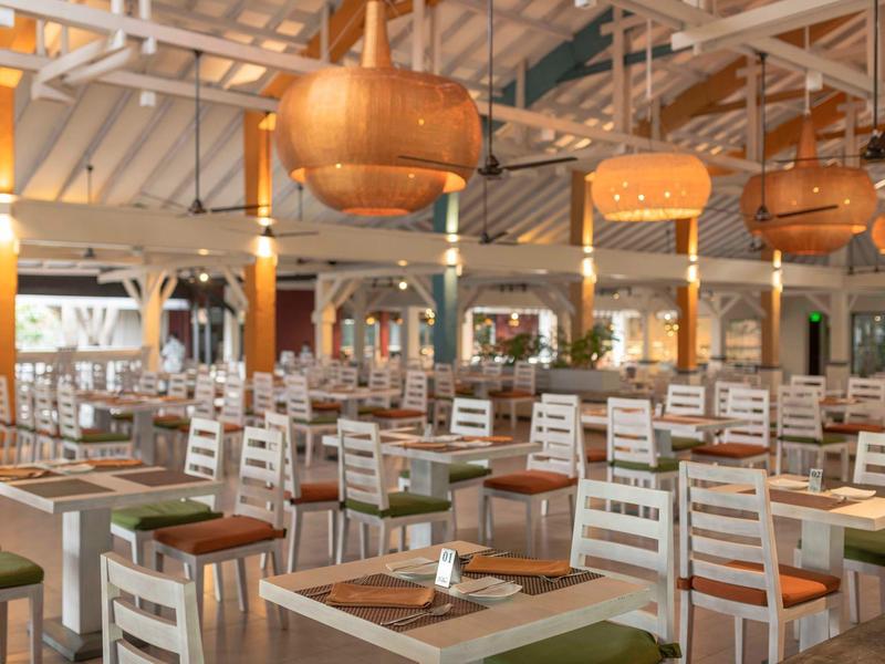 Spacious, bright dining room with white chairs, green cushions, and hanging round lamps.