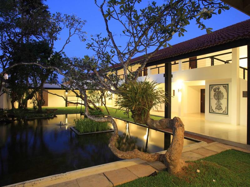 Avondzicht op een verlicht hotel met een vijver en bomen op de voorgrond.