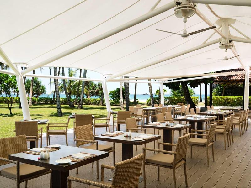 Buitenrestaurant met tafels en stoelen onder een groot wit zeil.