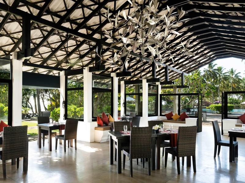 Open eetruimte met donker meubilair, witte zuilen en uitzicht op tropische tuin.