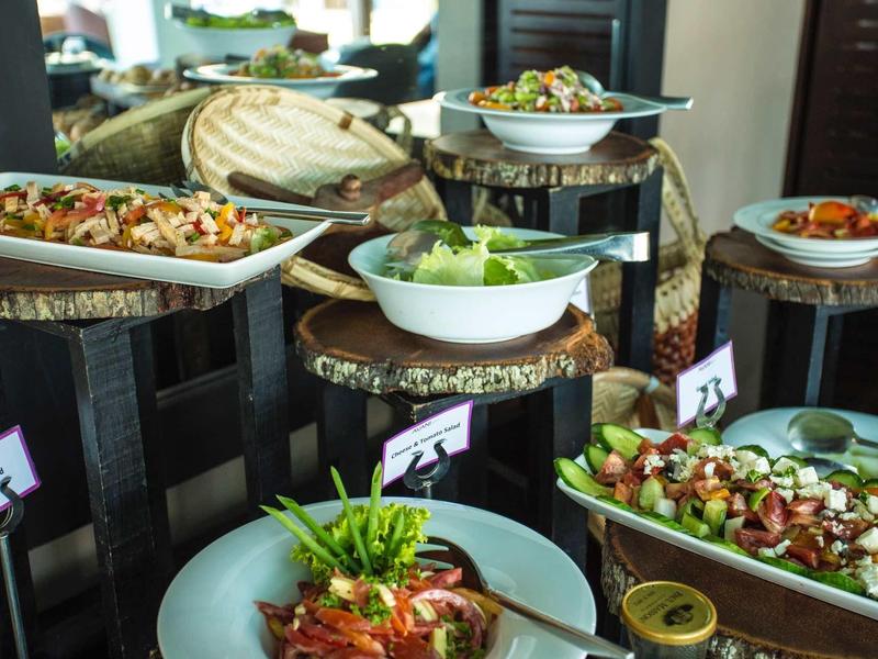 Buffet met verschillende salades en gerechten in witte kommen op rustieke houten planken.