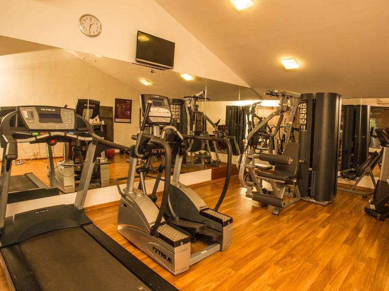 Fitnessruimte met loopbanden, trainingsapparatuur en houten vloer in een hotel.