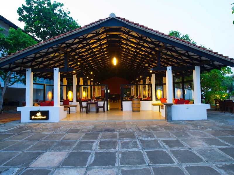 Open hotel lobby met dak en zitgedeeltes omgeven door bomen.