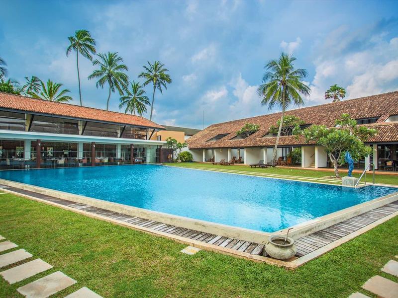 Groot zwembad met helder water, omgeven door palmbomen en gebouwen onder een zonnige lucht.
