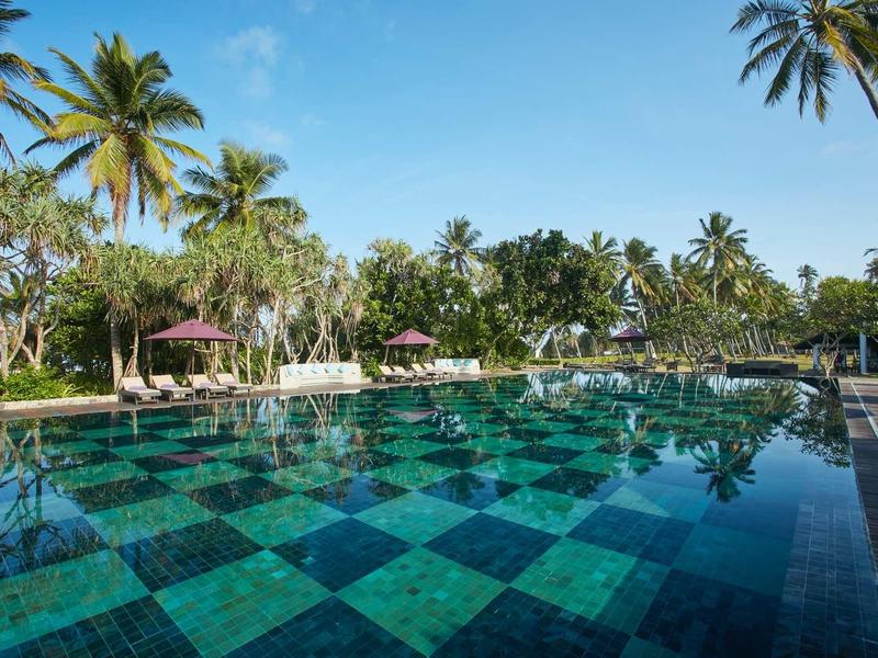 Zwembad met dambordvloer in een tropisch resort met palmbomen.