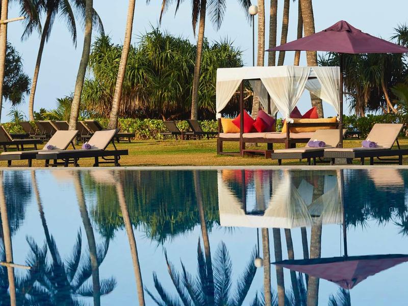 Luxe zwembad met ligstoelen, baldakijnbed en palmbomen op de achtergrond.