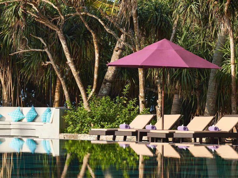 Zwembad met ligstoelen en een roze parasol voor palmbomen in de hotel tuin