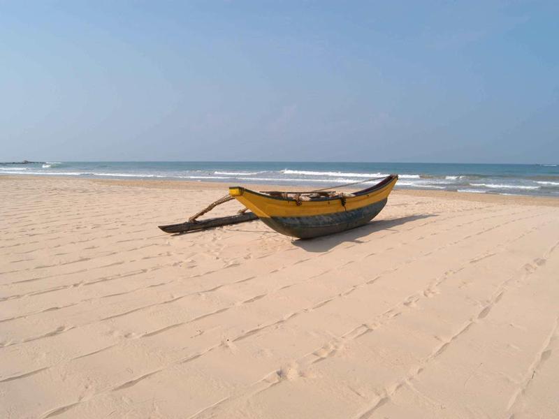Leeg bootje ligt op een breed zandstrand met rustige zee op de achtergrond.
