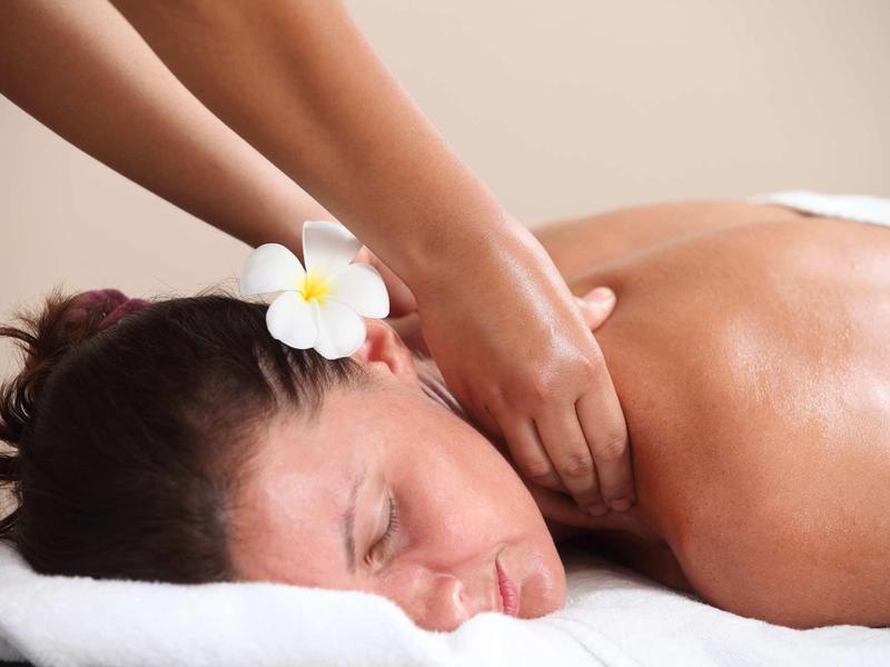 Vrouw ontspant tijdens nekmassage met witte bloem in haar op een witte tafel.