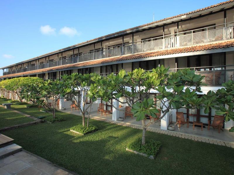 Modern hotelcomplex met twee verdiepingen, omringd door verzorgd gras en bomen.