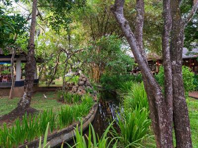 Grüner Garten mit Bäumen und kleinem Wassergraben neben Gebäuden.