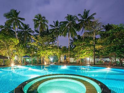 Beleuchteter Pool mit Palmen und Bäumen in tropischer Hotelanlage bei Abenddämmerung.