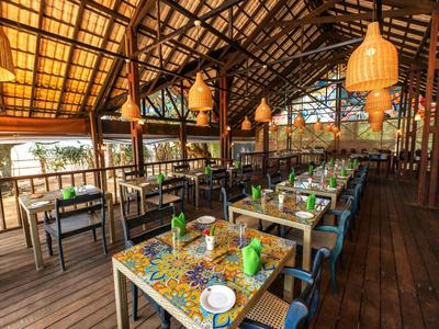 Offenes Restaurant mit Holzboden und bunten Tischen in tropischer Umgebung.