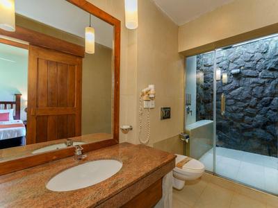 Helles Badezimmer mit Granitwaschbecken, großem Spiegel und begehbarer Dusche mit Natursteinwand.