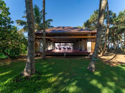 Ein Bungalow mit Veranda und Sonnenliegen, umgeben von Palmen und grünem Rasen.