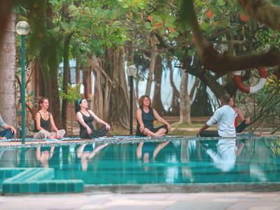 Menschen praktizieren Yoga am Rand eines Pools inmitten grüner Bäume.