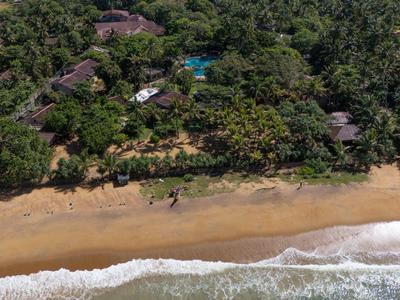Luftaufnahme des sandigen Strandes mit Wellen und bewaldetem Hotelbereich im Hintergrund.
