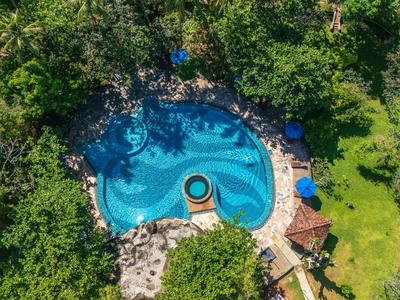 Luftaufnahme eines blauen Pool inmitten üppiger grüner Vegetation mit Liegestühlen und unbebauter Fläche.