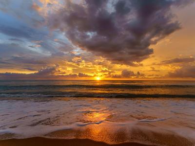 Sonnenuntergang über dem ruhigen Meer mit goldenen Reflexionen im Sand am Strand.