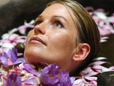 Frau entspannt im Wasser, umgeben von lila Blüten, in einem Spa- oder Urlaubsszenario.