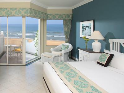 Chambre d'hôtel avec vue sur la mer, meubles blancs et balcon avec table et chaises.