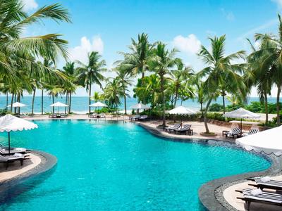 Grande piscine avec chaises longues et palmiers au bord de la mer dans une station tropicale.