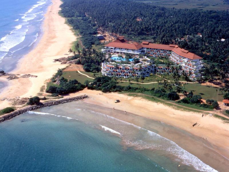 Vue aérienne d'un hôtel sur une longue plage de sable avec une forêt adjacente.