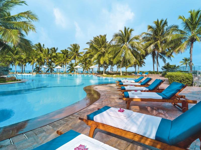 Chaises longues détendues près de la piscine avec des palmiers et un ciel bleu en arrière-plan.