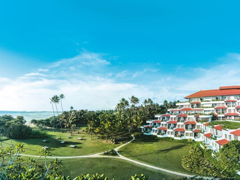 Complex de luxe aux toits rouges près d'une végétation luxuriante sous un ciel bleu au bord de la mer
