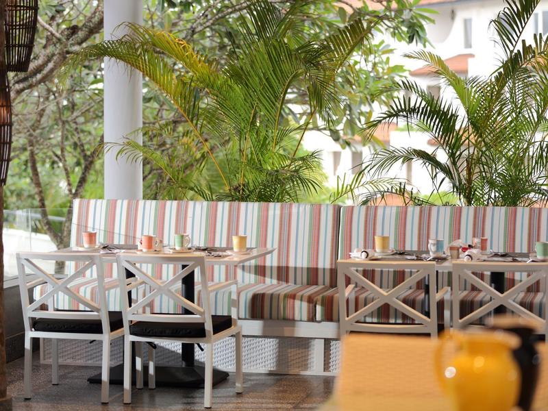 Coin repas extérieur confortable avec coussins rayés et palmiers en arrière-plan.