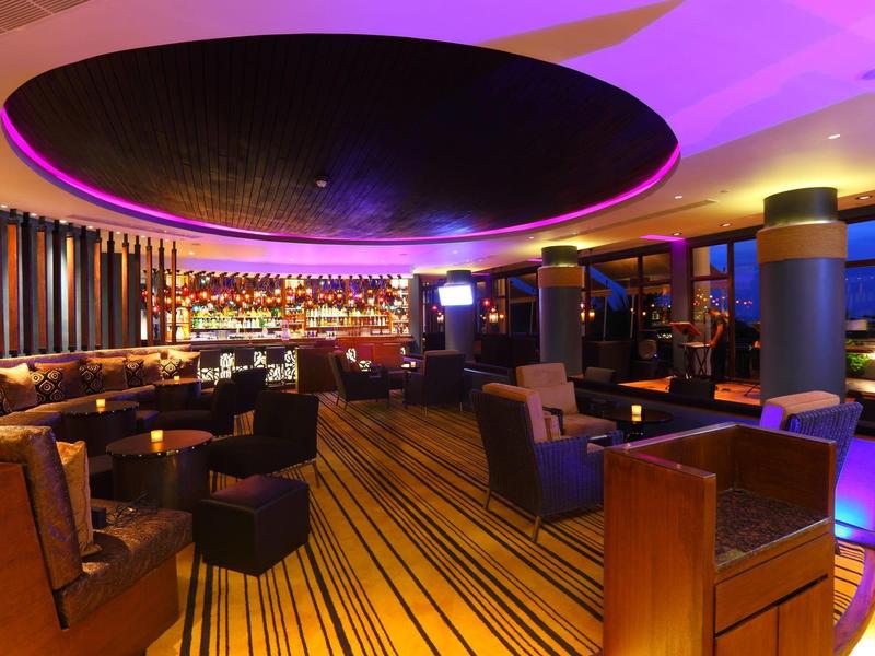 Bar d'hôtel élégante avec sièges stylés et éclairage coloré au plafond.