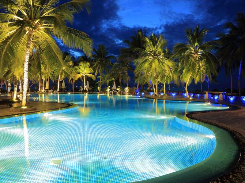 Piscine éclairée avec des palmiers la nuit dans une station tropicale.