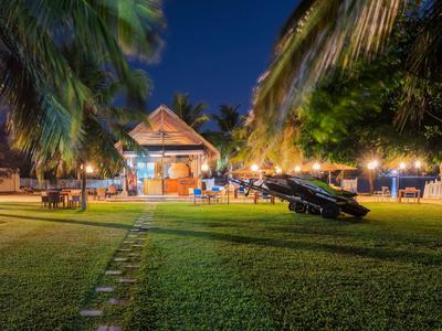 Grüner Garten mit Sitzbereich, Palmen und beleuchtetem Holzhaus bei Nacht.