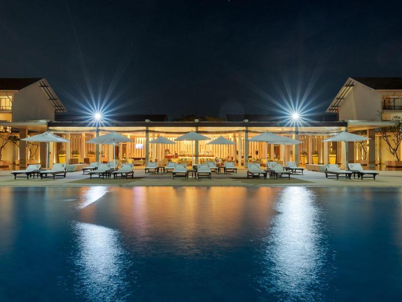 Verlicht zwembadhotel 's nachts met loungeruimtes en weerspiegelend water