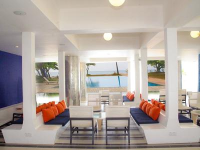 Moderner, heller Lounge-Bereich mit weißen Möbeln, blauer Wand und orangefarbenen Kissen am Meer.