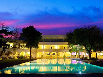 Beleuchtetes Gebäude mit Pool und Bäumen bei buntem Abendhimmel in Blau und Pink.